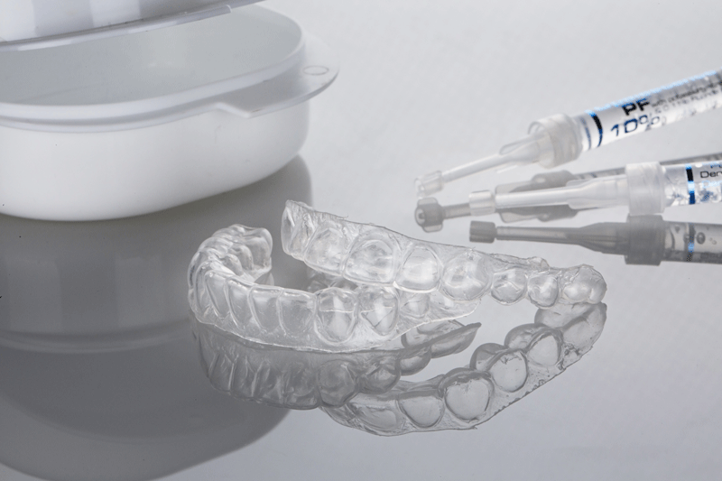 dental cap of the upper and lower jaws for whitening and syringes with whitening gel on a light background.