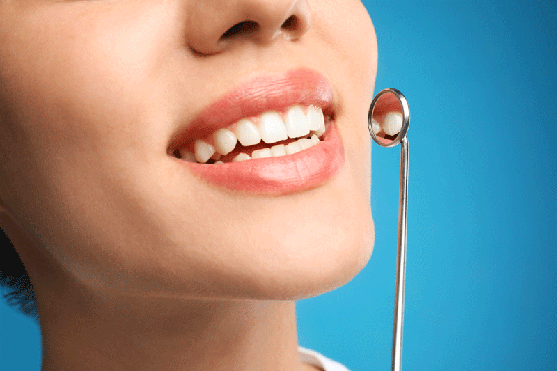 Young woman with mouth mirror on blue background, closeup. Cosmetic dentistry.